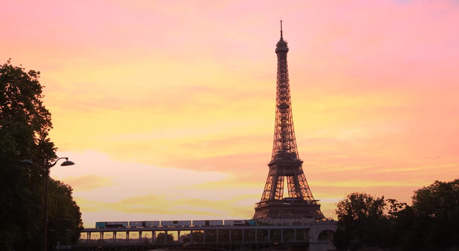 Video still: a train tagged 1UP crossing a bridge at sunset with the Eiffel Tower behind it