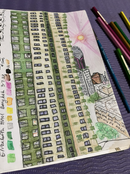 A sketch of an apartment building with uneven lines, the Bangkok city line is visible on the right side, foliage scattered between, the sky is pink and the sun is glowing brightly. Down the left side is a palette of the watercolor pencil colors used to create the scene. Thanks for checking it out and not making fun of it.