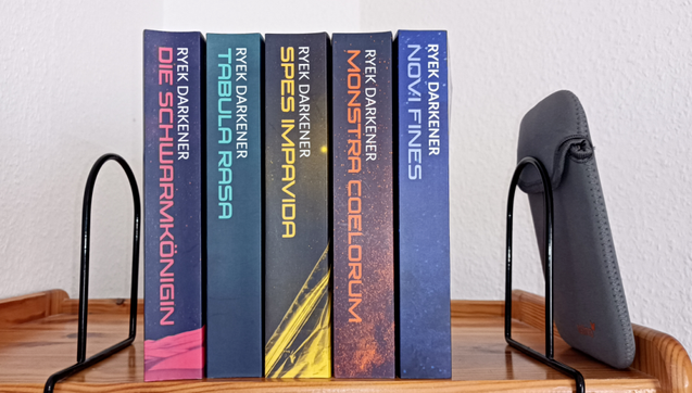 Das Bild zeigt ein Regal mit den Büchern der Reihe "Geschichten aus der Welt nach dem Letzten Krieg":

Die Schwarmkönigin
Tabula Rasa
Spes Impavida
Monstra Coelorum
Novi Fines

sowie einen E-Book Reader in einer Hülle.