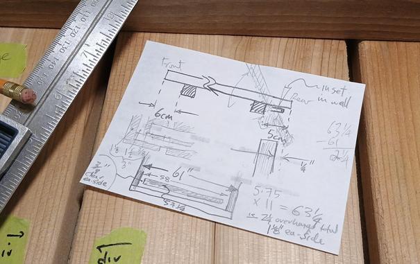A quarter sheet of scrap paper sits on some cedar slats and it's covered in dimensions and sketchy scribbles and various bits of arithmetic.