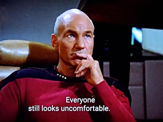 Star Trek The Next Generation scene. Captain Picard, a bald guy in a red uniform, is sitting on the bridge in his smooth puffy leather captain's chair and pondering with hand resting on chin. Caption reads, "Everyone still looks uncomfortable."