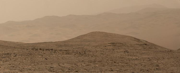 An ochre toned image capturing a Martian landscape, with the rim of Gale Crater in the background.