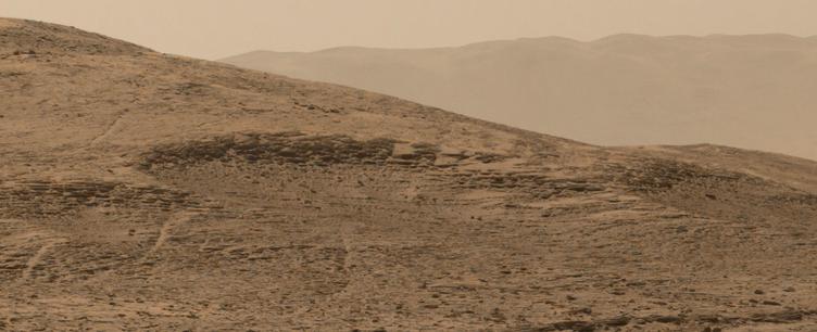 An ochre toned image capturing a Martian landscape, with the rim of Gale Crater in the background.