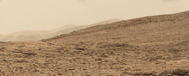 An ochre toned image capturing a Martian landscape, with the rim of Gale Crater in the background.