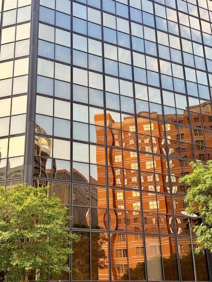 A brick building is reflected in the windows of a glass building