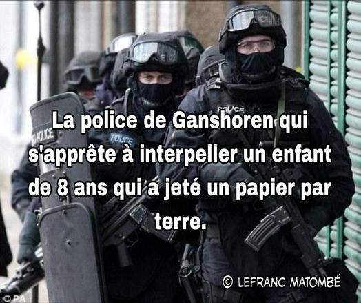 Des policiers lourdement armés en tenue d’intervention, avec casques, gilets pare-balles et boucliers, avancent dans une rue. La légende ironique superposée dit :
« La police de Ganshoren qui s'apprête à interpeller un enfant de 8 ans qui a jeté un papier par terre. »
Crédit : © LEFRANC MATOMBÉ.
