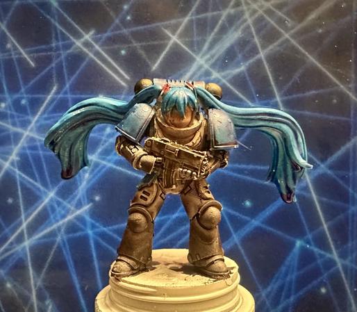 A Warhammer 40K Space Marine with the head of Hatsune Miku - impossible pigtails included. The marine armor is grey with black legs and blue shoulder pads, and Miku’s hair is her expected blue.