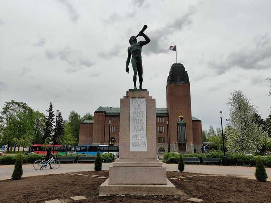 Joensuun parturoidun Vapaudenpuiston Paimenpoika-patsaan jalustassa riippuu juliste Kylvä pottua, älä miinoja! 