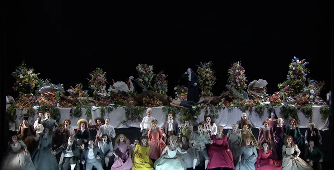 The chorus – about 40 people! – of Saul dressed in colourful regency clothes in front of a huge banqueting table covered in massive bouquets of flowers. A swan, a boar and a deer are stuffed full of overflowing fruits