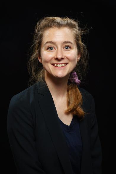 A photo of Amy looking happy, wearing a black blazer and a dark blue blouse.