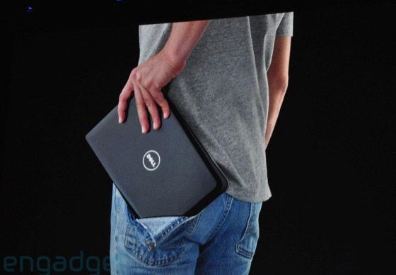 Foto parcial do corpo de um homem de pé, de costas, um pouco de lado, usando camiseta cinza e calça jeans e o bolso da calça está rasgando porque ele está tentando guardar um notebook
