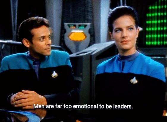Deep Space Nine scene. Jadzia Dax and Dr. Bashir are in their blue uniforms sitting in the operations center. Bashir is gazing lovingly at Dax. Dax is looking at something else entirely not named Bashir. Closed caption reads, "Men are far too emotional to be leaders."