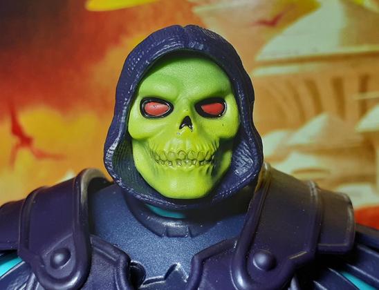 Another photo of the head and shoulders of the action figure Barbarian Skeletor. This time, Skeletor's head has been swapped for one that has a more classic look - a purple hood and no beard. Skeletor's face is a yellow skull with a greenish tinge. His eyes are red and surrounded by the black of his eye sockets.
