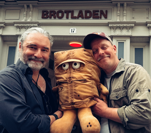 Norman Cöster und ich vor dem Brotladen in Erfurt, mit einer großen Bernd das Brot Plüschfigur zwischen uns. Ich lächle, Norman kuschelt sich an Bernd. 