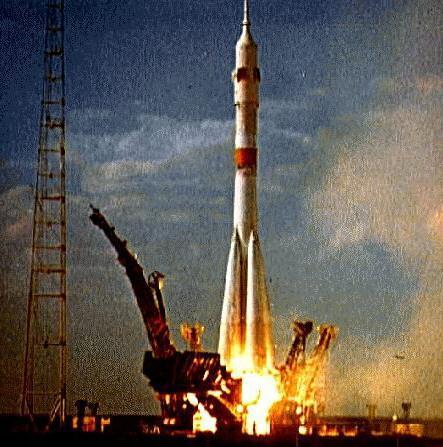 Photo of the Soyuz 9 rocket taking off from its pad. It has a central booster and four auxiliaries attached diagonally to the base—the standard configuration since the R-7 ICBM on which it was derived debuted in 1957.