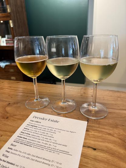 Three glasses of cider on a bar.