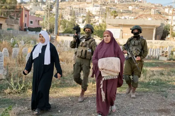 Two Israeli soldiers, with guns raised, escort two women out from a cemetery in Jenin.
