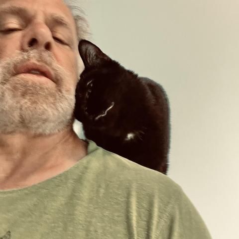 a black cat on a mans shoulder rubs his head against the man's cheek