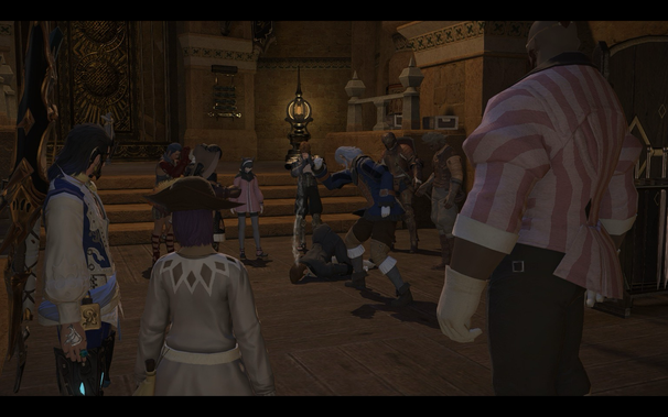 A scene from the video game Final Fantasy XIV. A group of anime-style characters stand in an ornate, dimly lit room, surrounding another character who is lying prone on the wooden floor. One character in a blue and white coat is shown kicking the fallen figure. The other characters look on, some with concern. A large, intimidating figure in a pink and white striped shirt partly obscures the view on the right side of the frame.