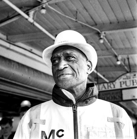 Black and white photo of a man wearing a white hat and a coat with the letters MC.