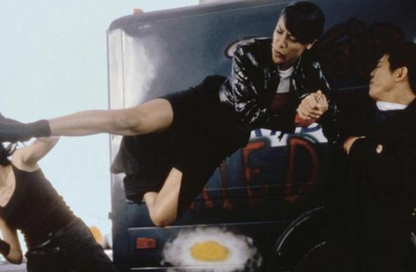 American musician, dancer and actress Aaliyah Haughton as Trish O’Day in the 2000 action romance film “Romeo Must Die”. She is wearing a dark leather jacket and a black skirt. She’s kicking someone in the face while being physically supported by Chinese-Singaporean martial artist and filmmaker Jet Li, who is wearing a dark colored shirt while holding her arm tightly. 