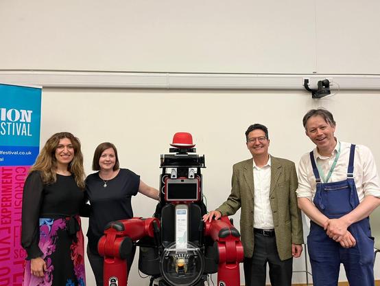 Four people posing for a photo with a red humanoid robot.