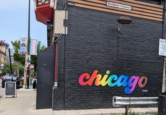 The side of a brick building, painted black. The word "chicago" is painted on the wall in bright rainbow colors which really pop against the painted brick.