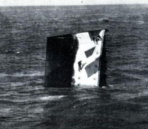 Barco hundiéndose, en posición vertical. Un hombre escala por fuera.