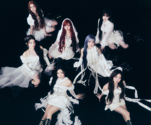 A promotional photo of the 7 remaining members of Kep1er for "Against The World", one of the group's Japanese releases. They are wearing ethereal clothes with lots of ribbons, half-long skirts, and sometimes even hoods. All of them are also wearing their hair long (with extensions if need be) to give them an added elegant look. They're sitting on a black floor, in a formation similar to that of a star or flower, looking up at the camera above them.