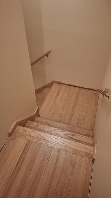 Looking down an oak stairs with a landing and turn to the left. The wood was sanded off and left it's natural color with a satin poly on top.