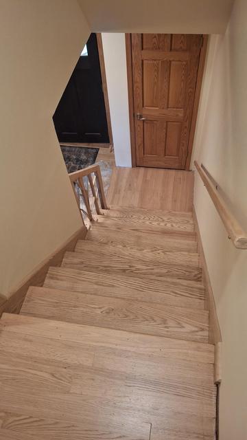 Looking down an oak stairs with a landing and turn to the left into the house entryway. The wood was sanded off and left its natural color with a satin poly on top.
