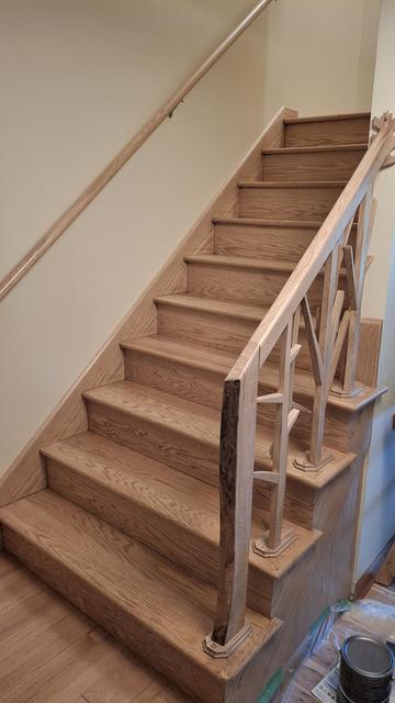 Looking up an oak stairs with a banister that resembles trees. The wood was sanded off and left it's natural color with a satin poly on top.