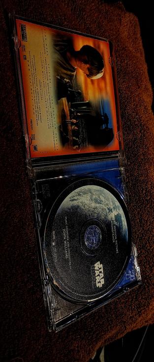  The photograph shot with 85F warming light, shows an open DVD case of "Star Wars: Episode I - The Phantom Menace." The case is placed on a brown textured surface, likely a carpet or fabric. The top half of the case displays the DVD cover, featuring a sunset scene with a character in the foreground and a spaceship in the background. The cover includes the title "Star Wars: Episode I - The Phantom Menace" and lists the main cast: Liam Neeson, Ewan McGregor, Natalie Portman, and others. The bottom half of the case contains the DVD disc, which is black with a textured surface and the "Star Wars" logo in the center. The disc also has the text "Original Motion Picture Soundtrack" and "Music Composed and Conducted by John Williams." The case is clear plastic, allowing the disc and cover to be visible.

 Ovis2-8B

🌱 Energy used: 0.220 Wh