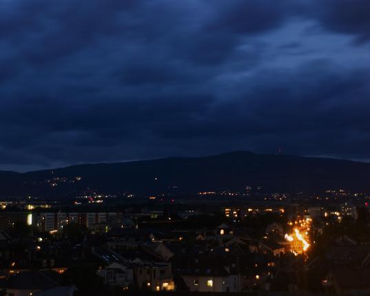 View of parts of Frankfurt at night. A main roads with bright lights on the right side of the frame, a forest clad hill with a radio tower on it in the distance. Clouds rushing by causing a blurry look.