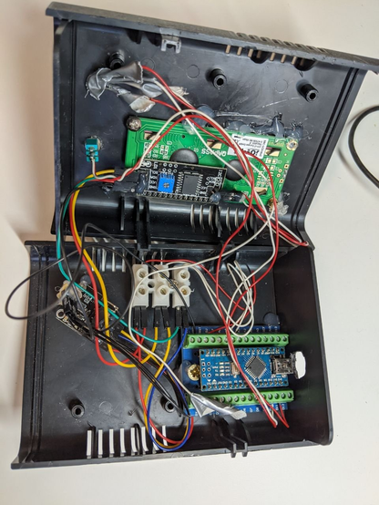 **TL;DR:** Final or near-final version of the AirMaster3000, enclosed in a black plastic case with neatly organized components and wiring.

**Extracted Text:**

* The green PCB reads: "anpress" and "[www.anpress.de](http://www.anpress.de)"

**Description:**
This is a close-up of the internal hardware of the AirMaster3000 CO₂ sensor housed inside a black plastic enclosure. The inside reveals an Arduino Nano on a breakout board with screw terminals, a green LCD module, a small PCB labeled “anpress”, and a tangle of red, black, and colored jumper wires. Components are secured with tape and glue, suggesting a DIY but functional approach. The setup shows progress from a prototype toward a deployable, enclosed version.
