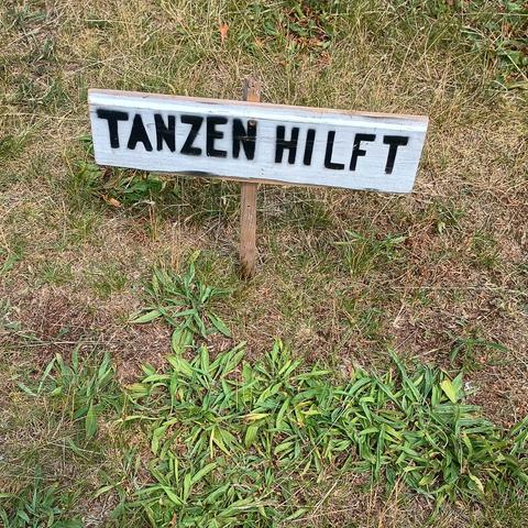 Ein kleines Schild auf einer Wiese mit der Aufschrift "Tanzen hilft"
