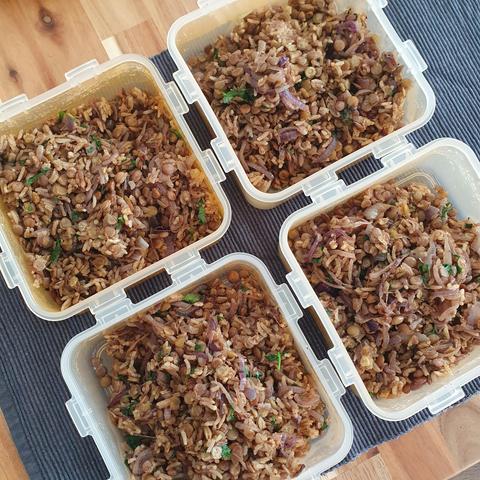 Four plastic lunch container wirh a dish consisting od lentils, rice and fried onions wirh some green cilantro mixed in. 