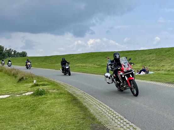 Motorräder fahren hintereinander am Deich entlang. 