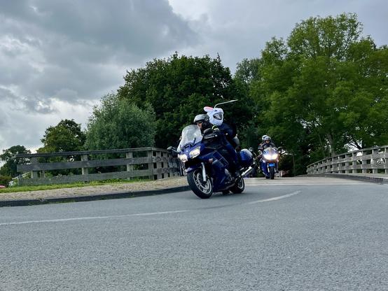 Motorräder fahren über eine kleine Brücke und biegen ab. 