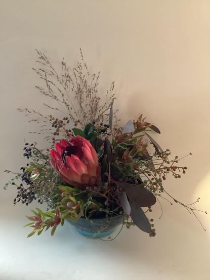 Ebendiese Schale gefüllt mit Blumen. In Zentrum steht eine rosa Protea.