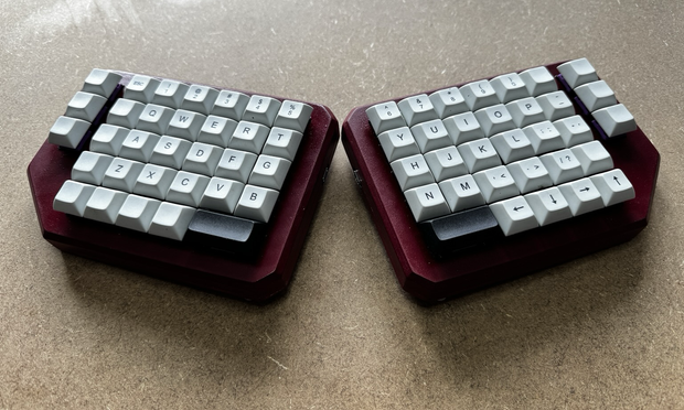 A mechanical keyboard with two split halves using an ortholinear layout. Each side has a six by five grid of keys with three additional keys on the outside edge.