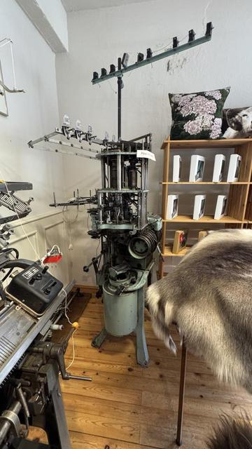 Also at Alafoss yarn shop; the v-bed machine in the previous picture is visible at the left edge of this one. This picture shows a vintage industrial circular sock-knitting machine with ribbing cylinder and a slew of yarn feeders — would be appropriate for making patterned socks mostly automatically. Again, it looks like it hasn’t been operated recently but it probably could be. 