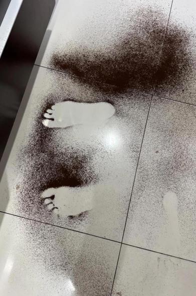 some sort of black dirt or dust with the imprint of two feet standing on a tile floor.