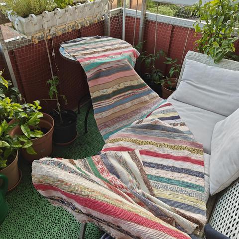 A striped woven rug from rags is draped over a sofa in a balcony.