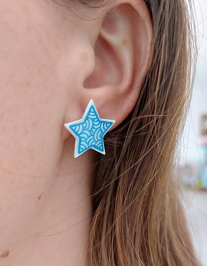 Puces d'oreilles fantaisie éco-responsables en forme d'étoiles blanches ornées de volutes bleues métallisées.
Les perles sont réalisées en CD recyclé, découpées et peintes à la main, puis recouvertes de résine époxy.
Les tiges sont en acier inoxydables.