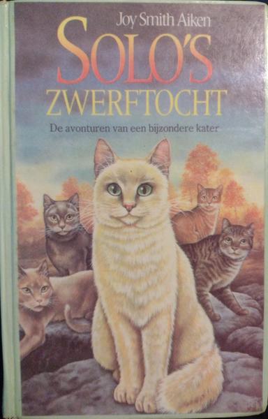 Voorkant van het boek "Solo's zwerftoch" van Joy Smith Aiken. Er staat een plaatje op van een zittende cremekleurige kat met meerdere andere katten op de achtergrond.