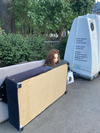Auf einem Haufen Sperrmüll neben einem Glascontainer, dessen Aufschrift das Abstellen von Abfällen verbietet, thront der lächelnde Kopf einer Schaufensterpuppe.