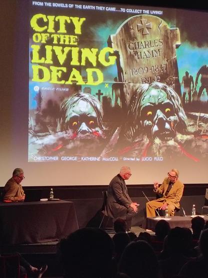 Mark Kermode talking to Simon Pegg as the poster for 1981 horror film City of the Living Dead is on the cinema screen behind them.