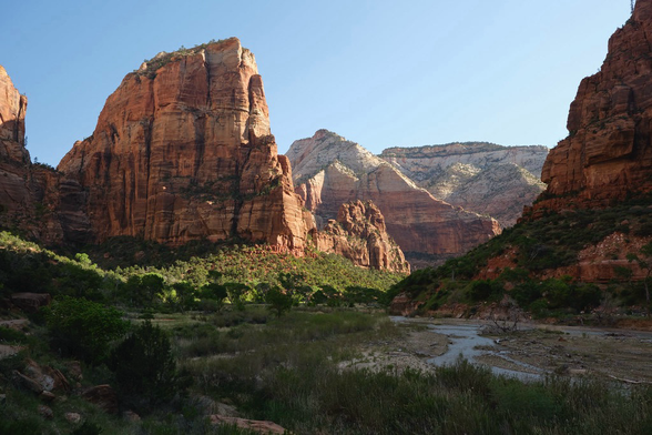 Main canyon of Zion on a cloudless day. Talk cliffs of red rock above a green valley floor. 