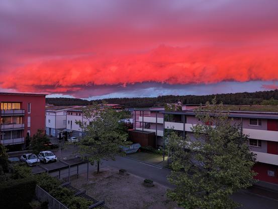 Ein Blick über Häuser hinweg auf wetterbedingt außergewöhnlich rot gefärbte Wolken in der Abenddämmerung.